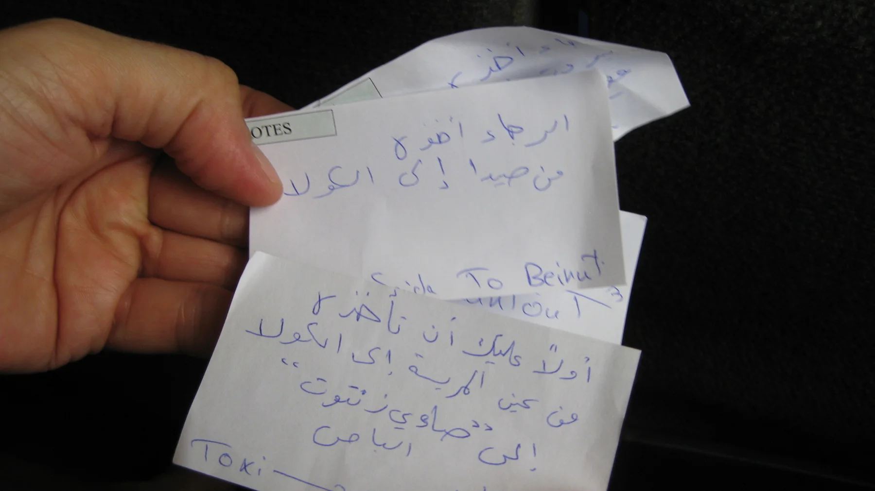 A hand holds a creased piece of paper covered with handwritten notes against a dark background.