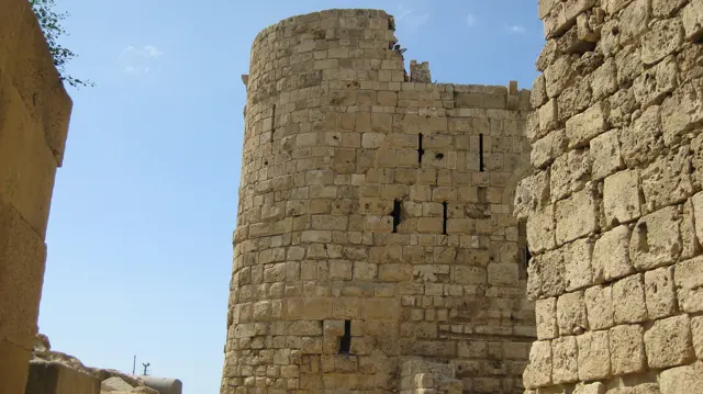 A rounded masonry tower with narrow openings rises between weathered walls against a clear blue sky.