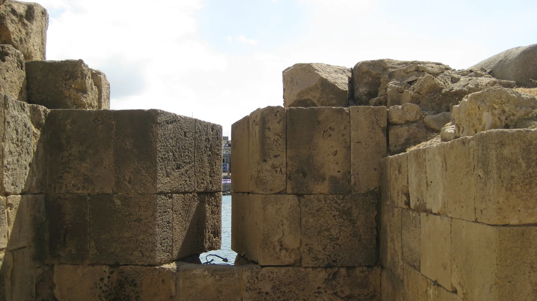 A slim vertical opening between large masonry blocks reveals a glimpse of water beyond.
