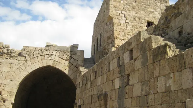 A large stone arch opens into darkness beside a rising masonry wall and rough steps.