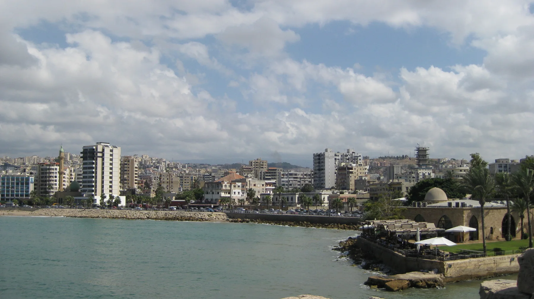 A dense waterfront skyline stretches across a bay beneath scattered clouds, with a domed building near the shore.