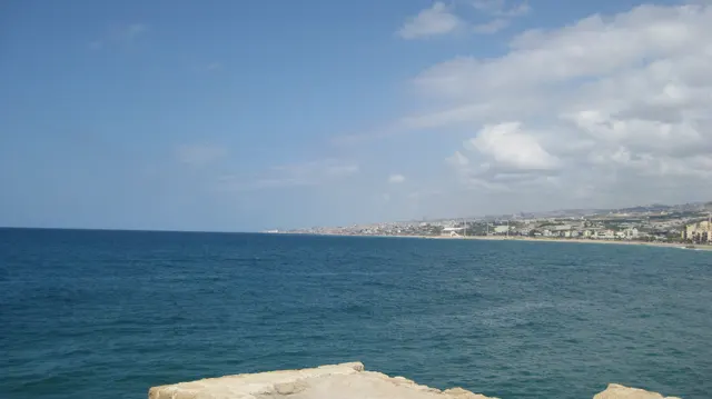Open blue water fills the foreground, with a low distant coastline beneath a lightly clouded sky.