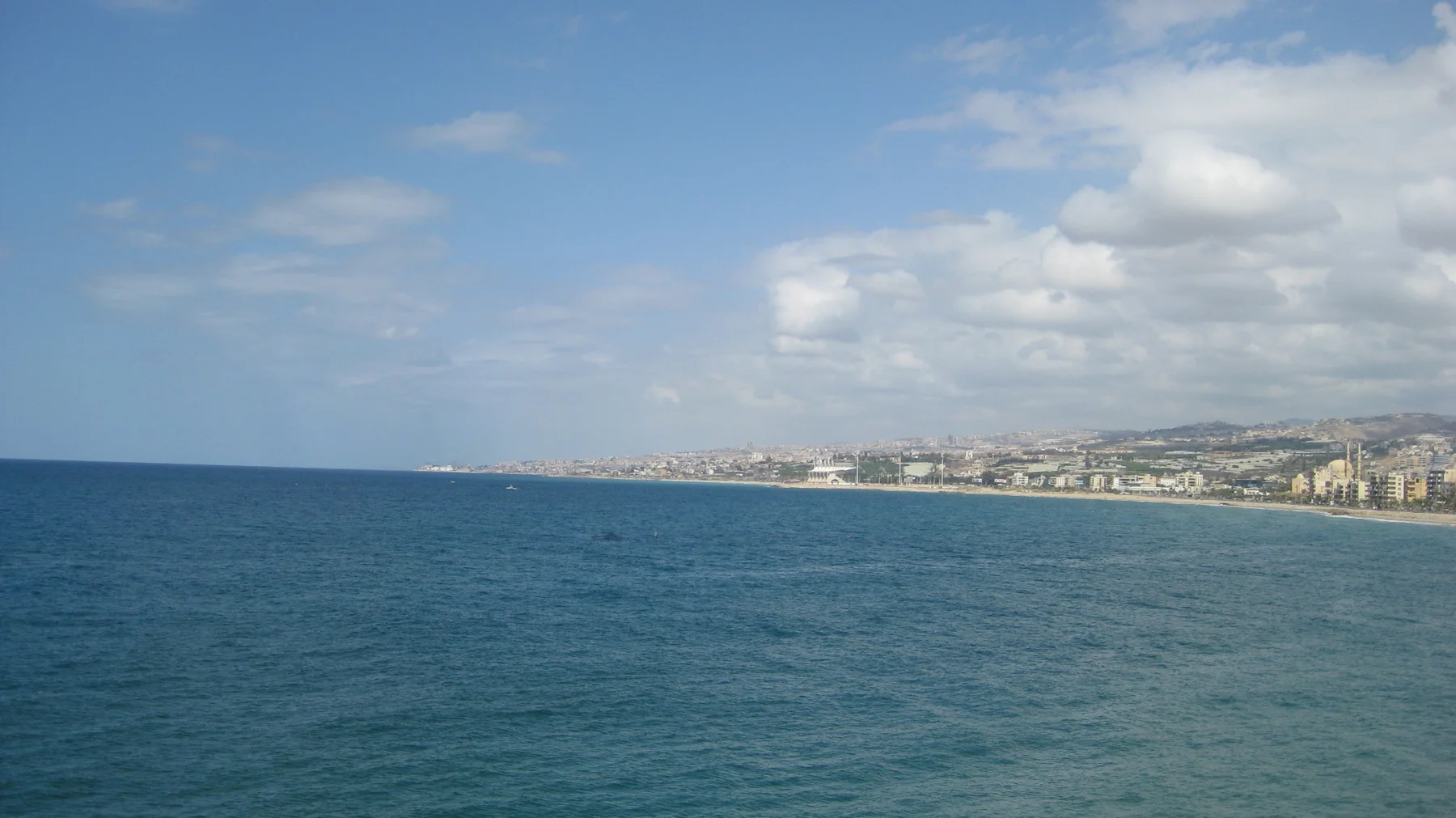 Deep blue water stretches towards a low coastline beneath a bright blue sky.