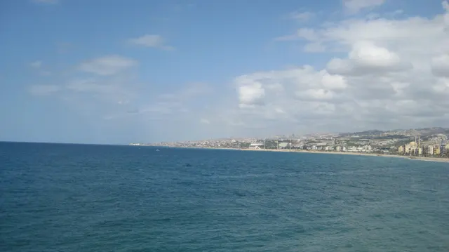 Deep blue water stretches towards a low coastline beneath a bright blue sky.