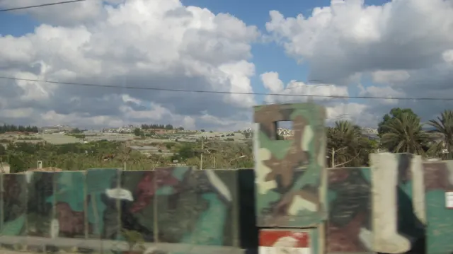A low wall painted in irregular green and brown patches crosses the foreground beneath utility wires.