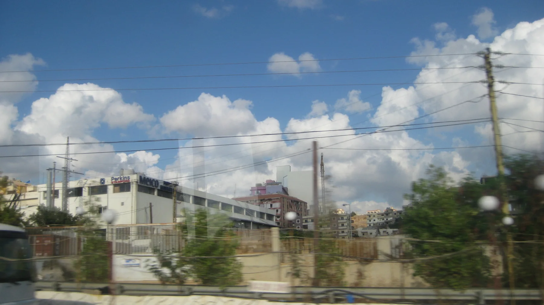 Utility poles and numerous wires cross a view of unfinished buildings and vegetation.