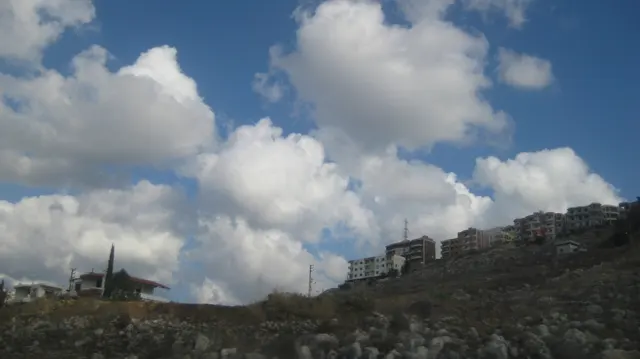 A dry hillside and sparse buildings form a low skyline beneath towering white clouds.
