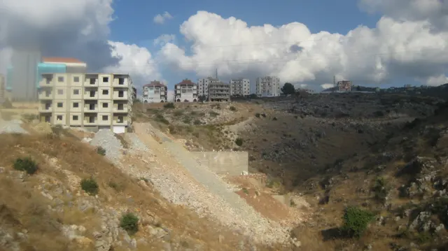 A pale multi-storey building stands above a steep exposed slope dotted with sparse vegetation.