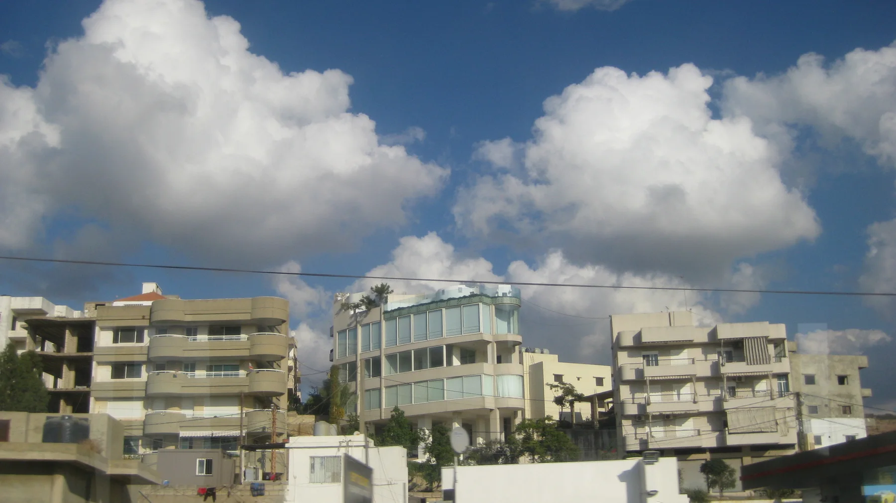 Several buildings with balconies and broad windows stand beneath large clouds and overhead wires.