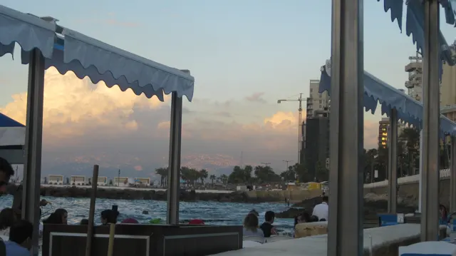 A blue-edged awning frames water and softly lit clouds beyond a seaside terrace.