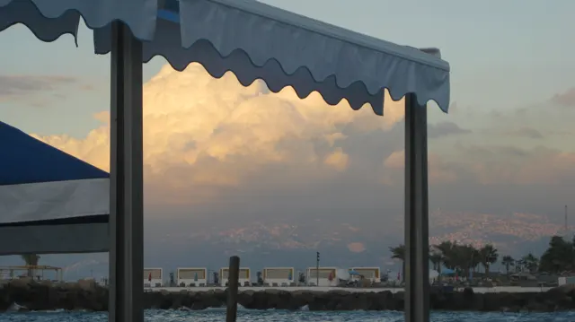 A scalloped awning and vertical supports frame warm-lit clouds over the waterfront.