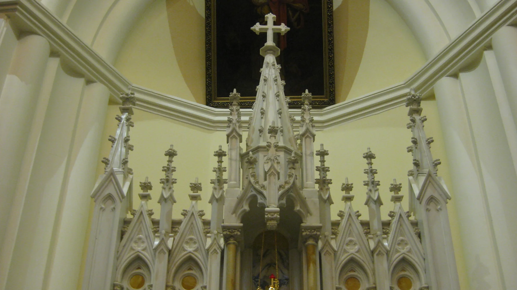 A richly decorated white altar with pointed spires and a cross stands beneath a pale church arch.