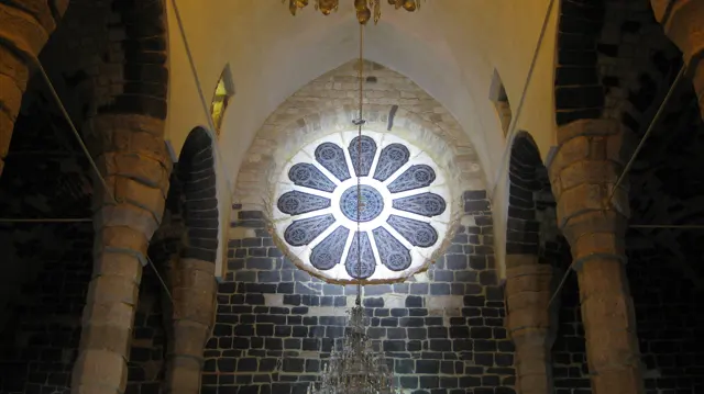 A bright rose-shaped window sits above an arch framed by dark stone columns.