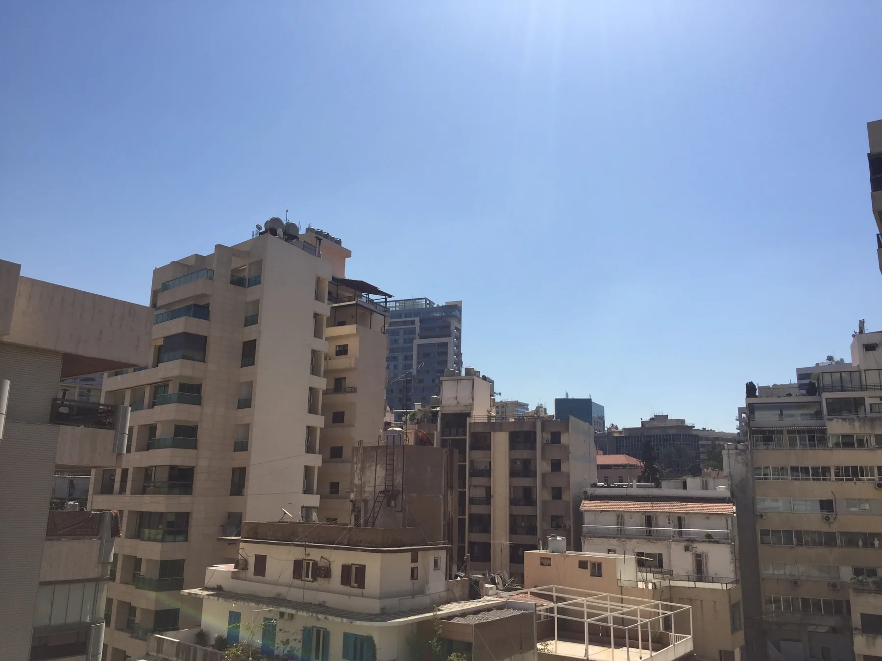 Closely spaced apartment buildings fill a sunlit urban view beneath a clear sky.