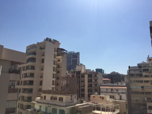 Closely spaced apartment buildings fill a sunlit urban view beneath a clear sky.