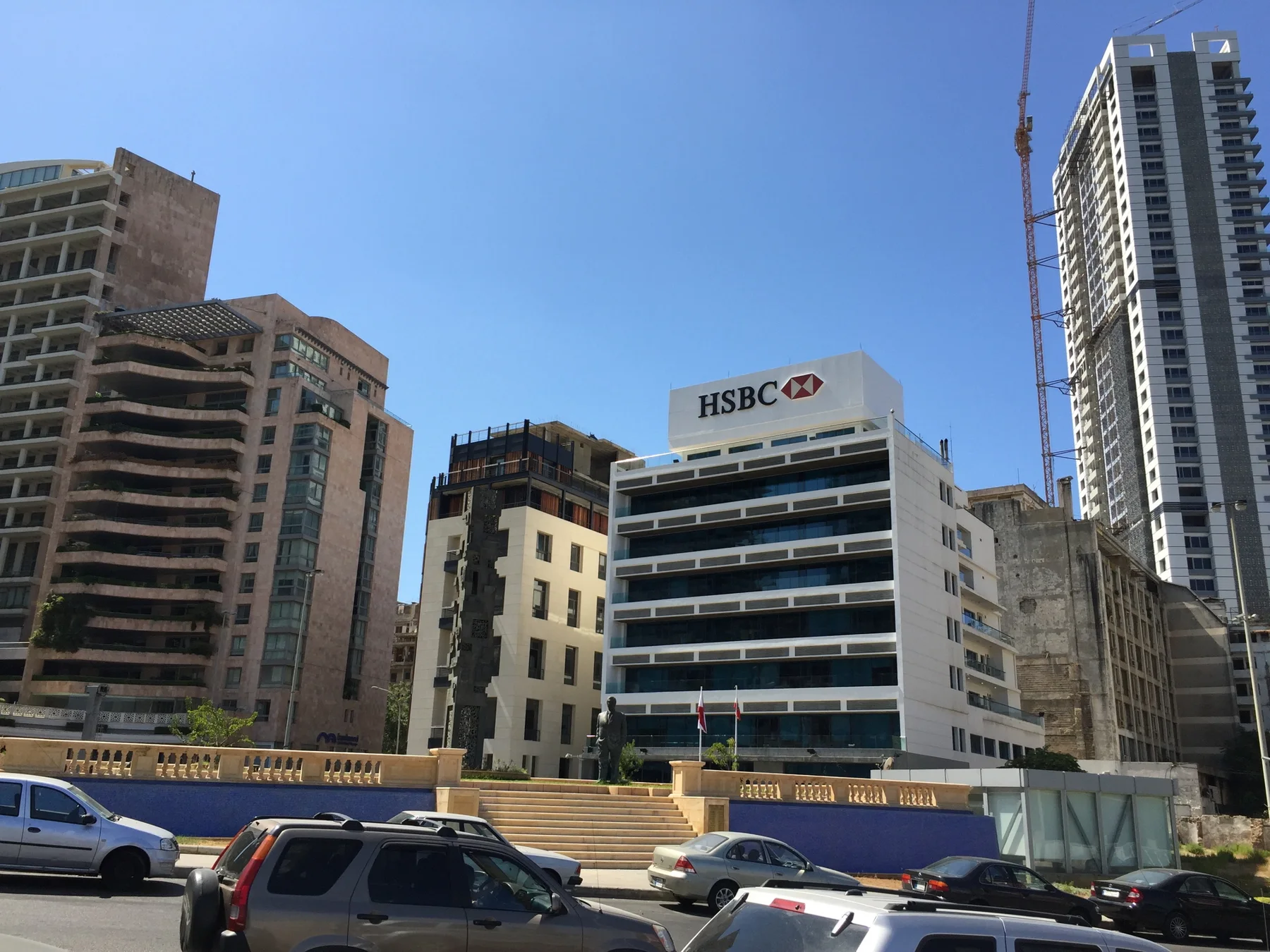 Tall office buildings and a lower bank facade stand behind a busy road.