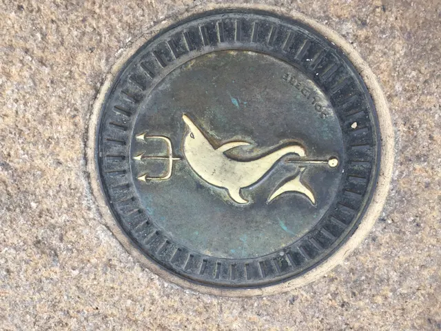 A round metal pavement cover bears a raised bird motif within a patterned border.