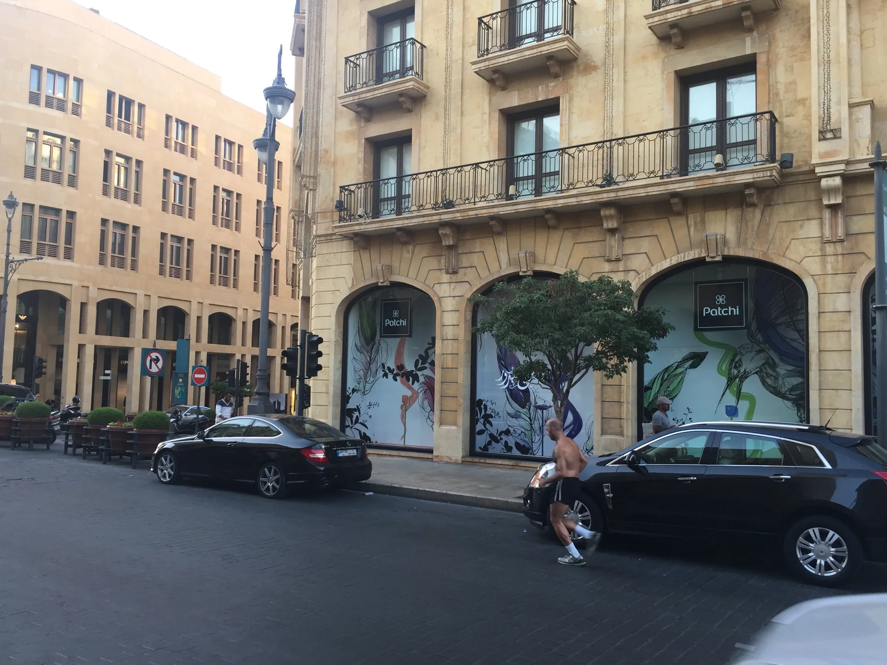 Parked cars line an ornate building with balconies and broad arched ground-floor windows.