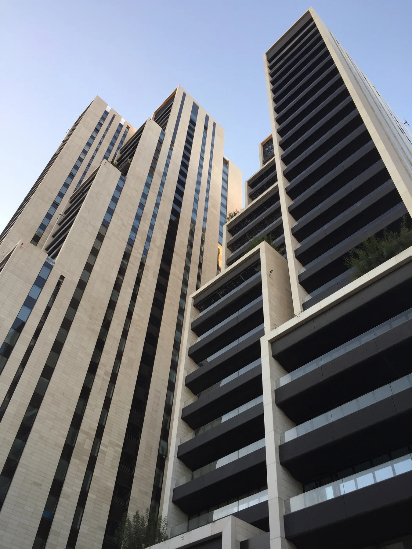 An upward portrait view follows tall ribbed building facades and stacked balconies against a blue sky.