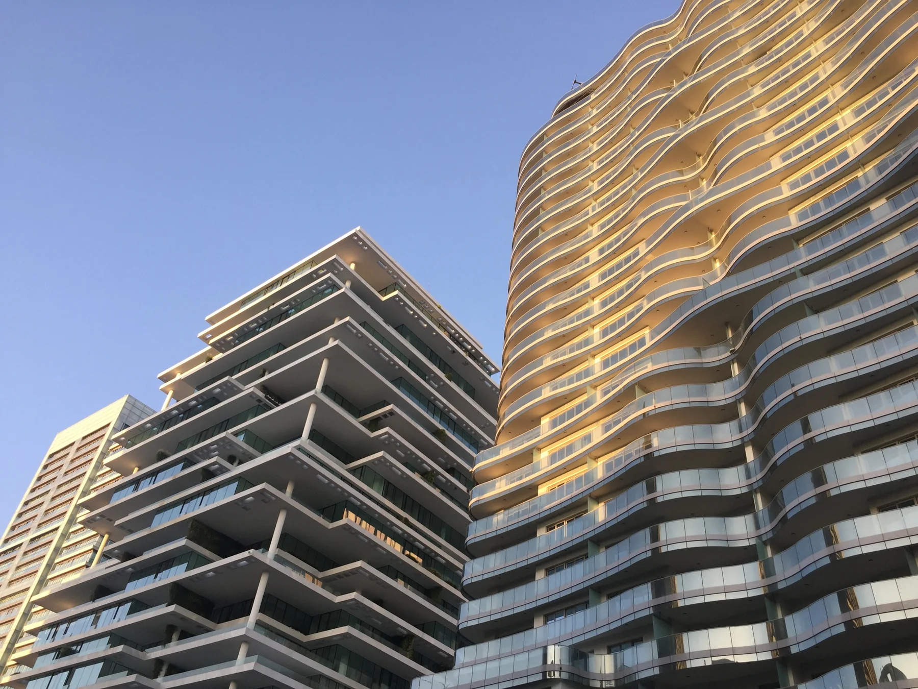 Warm light catches curved balcony edges on a tall building beside another with broad angular terraces.