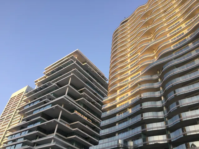 Warm light catches curved balcony edges on a tall building beside another with broad angular terraces.