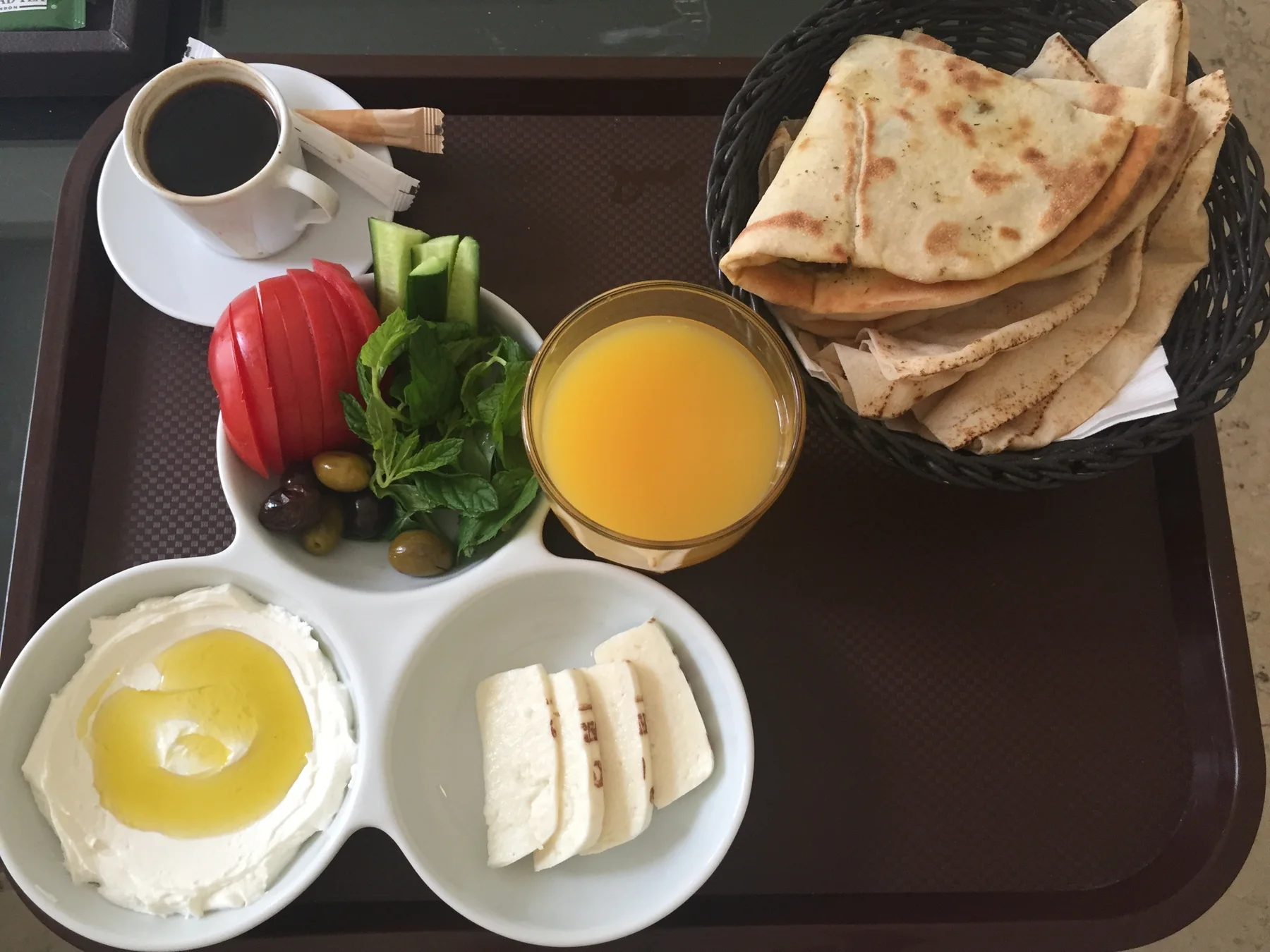 Flatbread, sliced vegetables, white cheese, small dishes, juice and a hot drink are arranged on a tray.