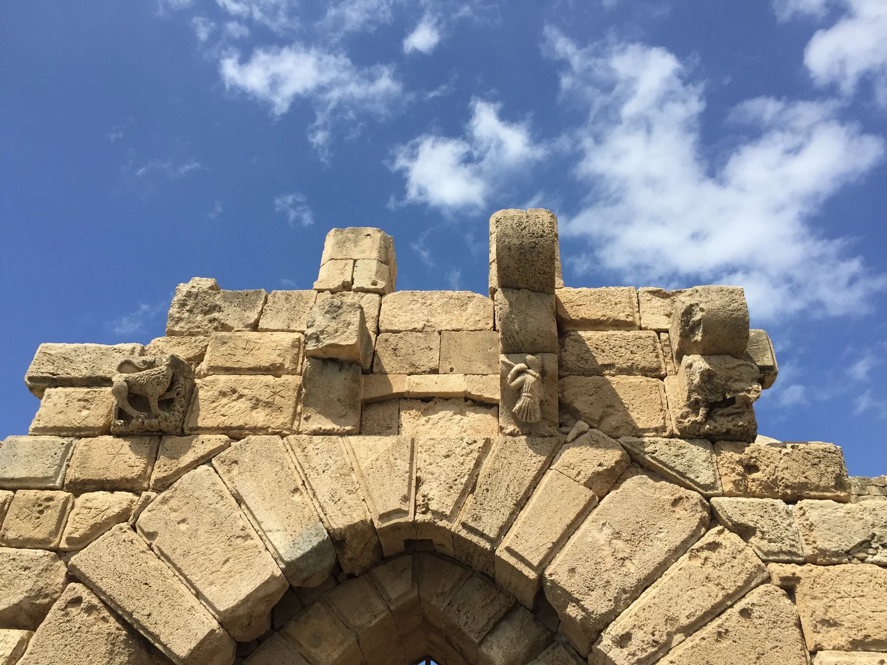 Large weathered blocks and projecting stones rise above a pointed entrance arch against the blue sky.