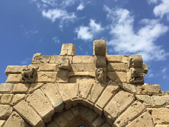 Large weathered blocks and projecting stones rise above a pointed entrance arch against the blue sky.