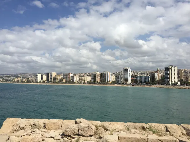 Waterfront buildings stretch across a turquoise bay, with pale stone at the lower edge.