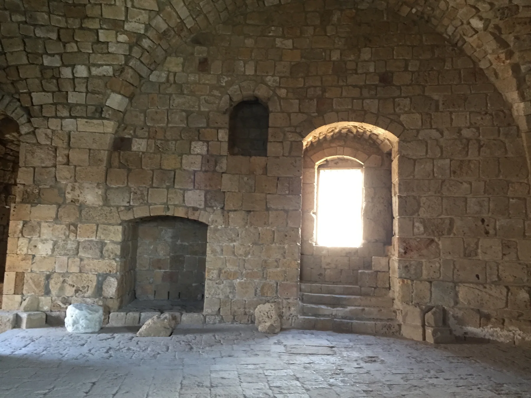 Sunlight enters through a narrow arched opening in a stone chamber with a vaulted ceiling.