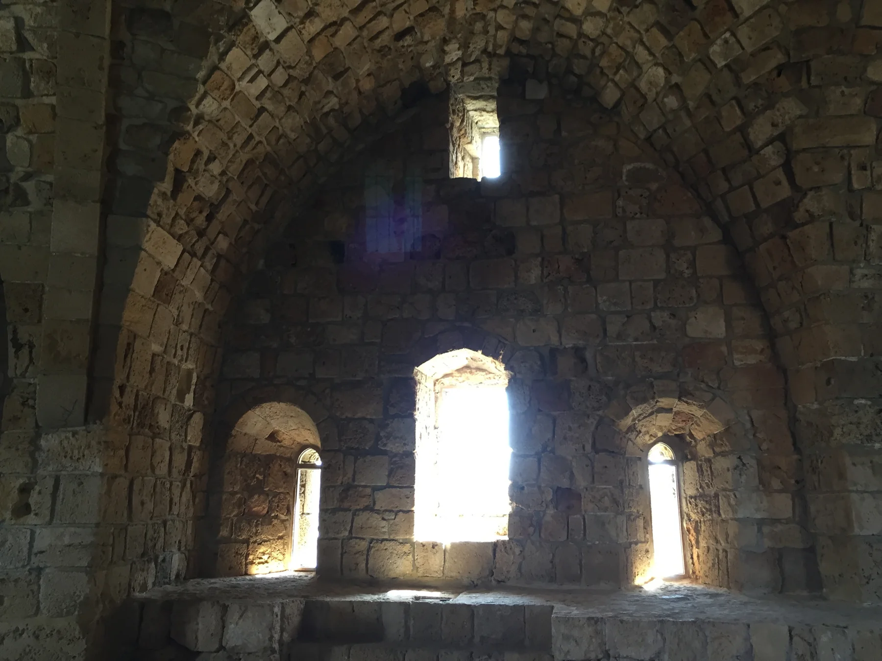 Bright arched windows punctuate a curved masonry wall beneath a dark vaulted ceiling.
