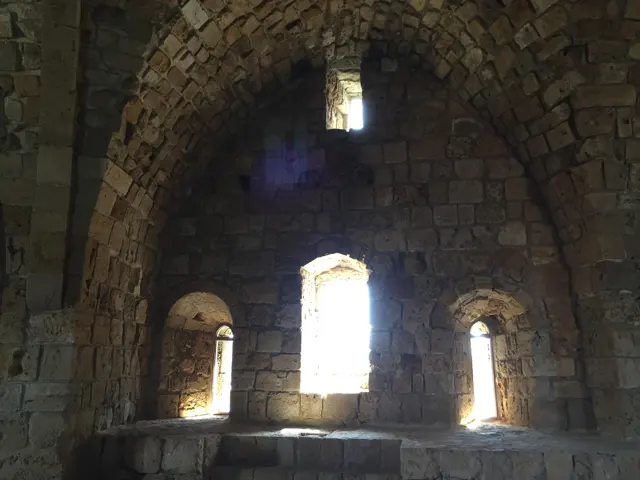 Bright arched windows punctuate a curved masonry wall beneath a dark vaulted ceiling.