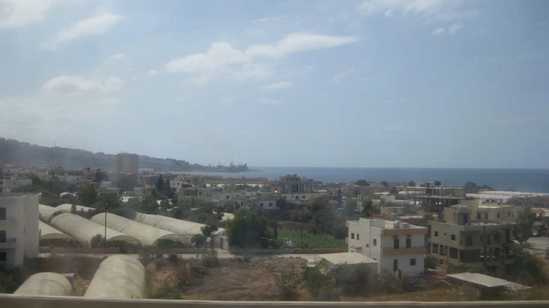 Low buildings and pale curved roofs spread towards the water in a hazy elevated roadside view.