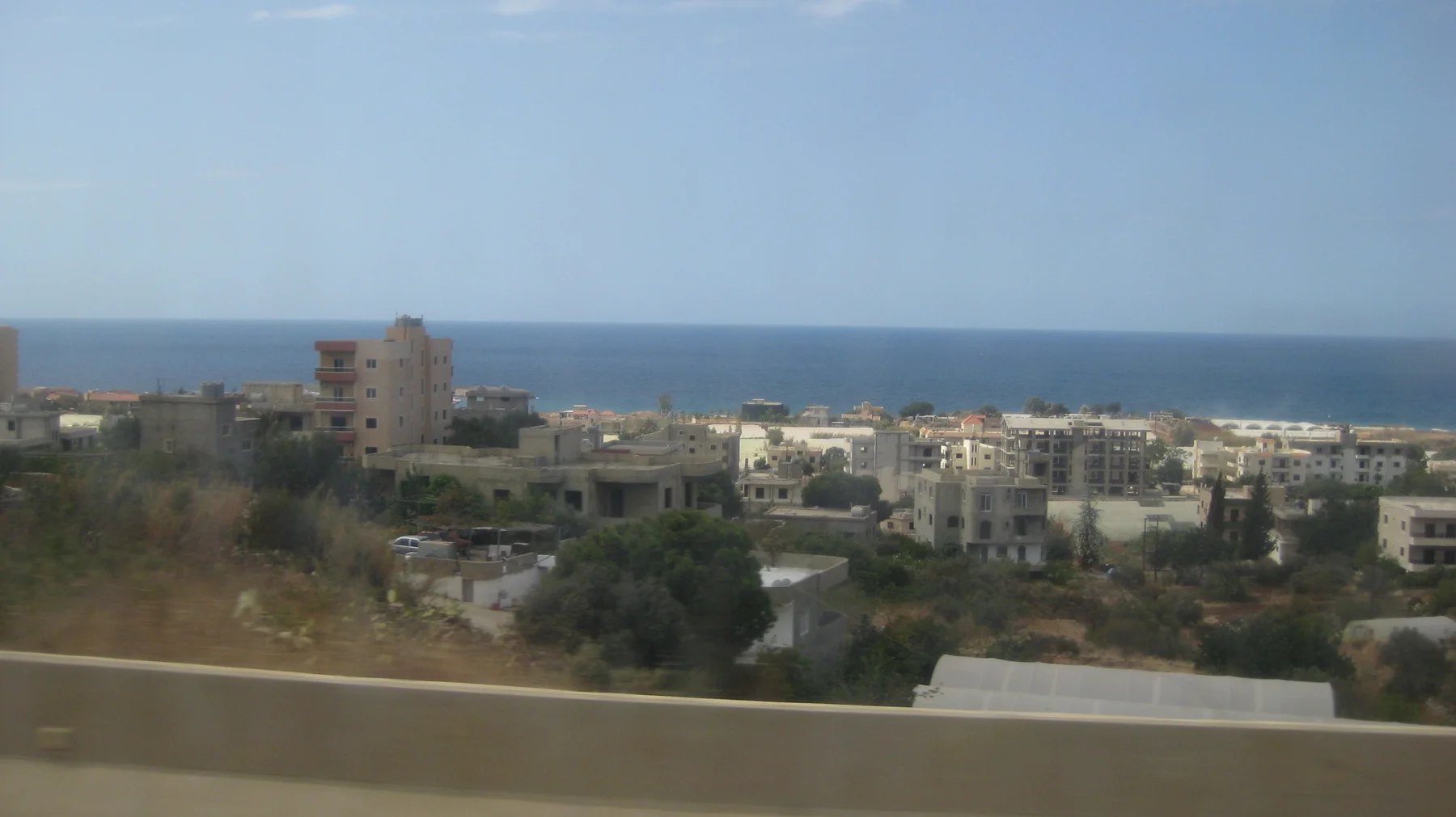 Buildings and patches of greenery fill the foreground below a long blue sea horizon.