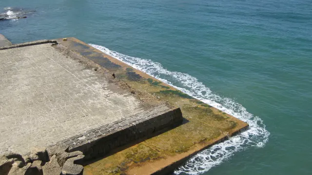 Blue-green water laps against a broad paved stone platform at the foot of the castle.