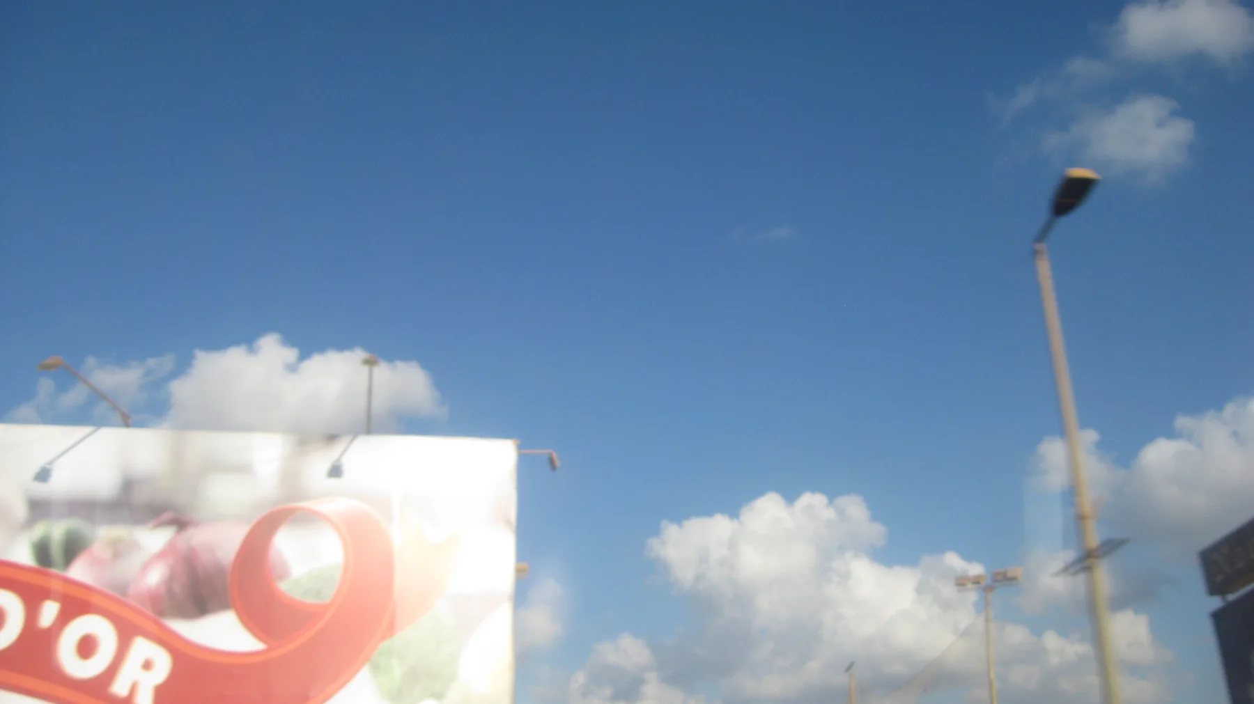 A partly visible advertising board and a tall lamp post pass beneath a bright blue sky.