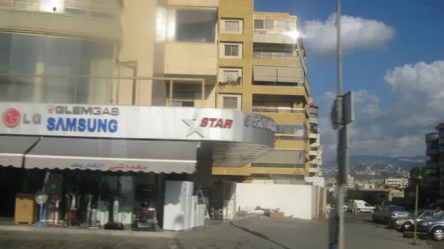 Large appliance-brand signs run across a shopfront beneath a yellow apartment building.
