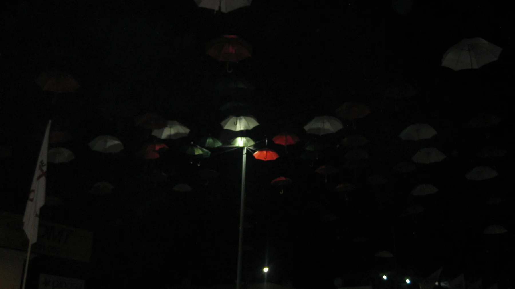 A street lamp picks out a few suspended umbrellas against a nearly black night sky.