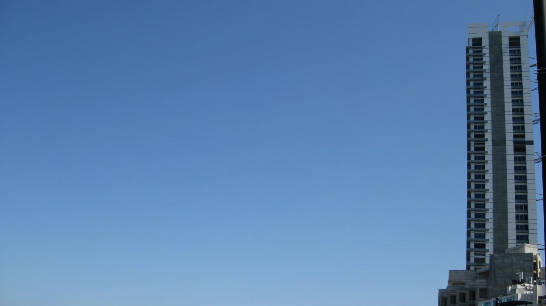 A narrow high-rise occupies the edge of a wide frame filled with clear blue sky.