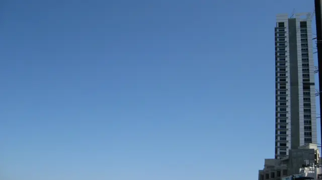 A narrow high-rise occupies the edge of a wide frame filled with clear blue sky.