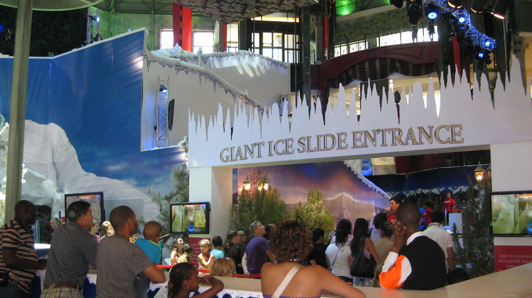 Visitors gather beneath a Giant Ice Slide Entrance sign with icicle-shaped decoration inside a shopping centre.
