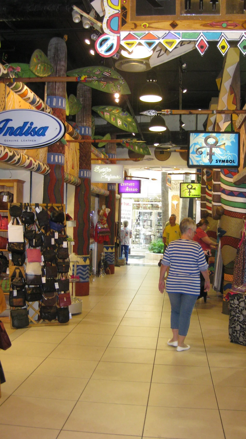 A person walks along an indoor shopping passage lined with colourful signs, displays and overhead decorations.