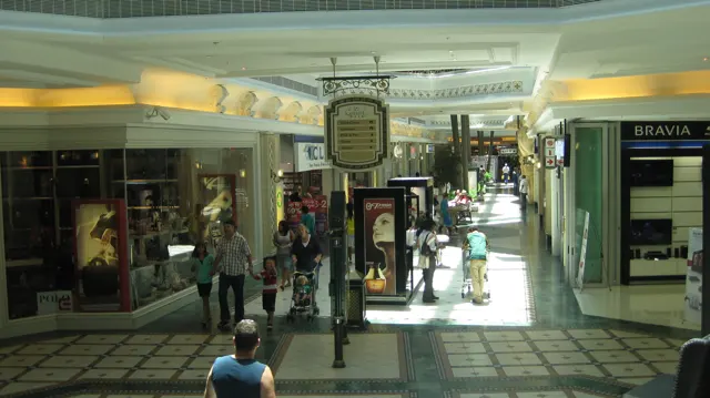 People walk between shopfronts along a patterned tiled passage, with daylight falling across the floor.