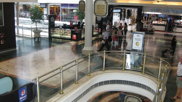 A curved upper-level railing overlooks a shopping-centre atrium, with shopfronts and visitors beyond.