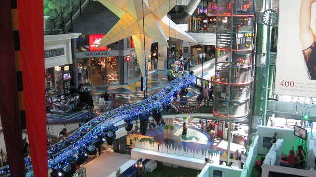 A large hanging star, a glass lift and a blue-lit truss fill a busy multi-level shopping-centre atrium.