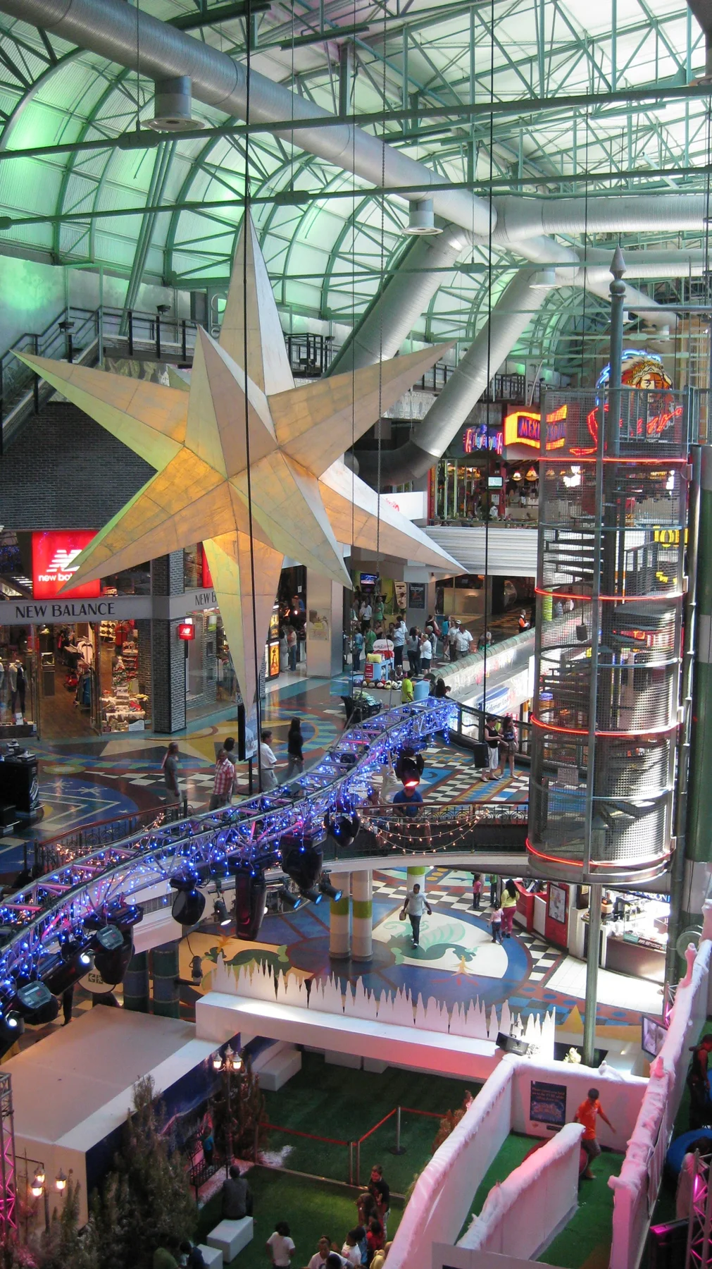 A portrait view looks across an atrium with a hanging star, a glass lift and illuminated decoration under a glazed roof.