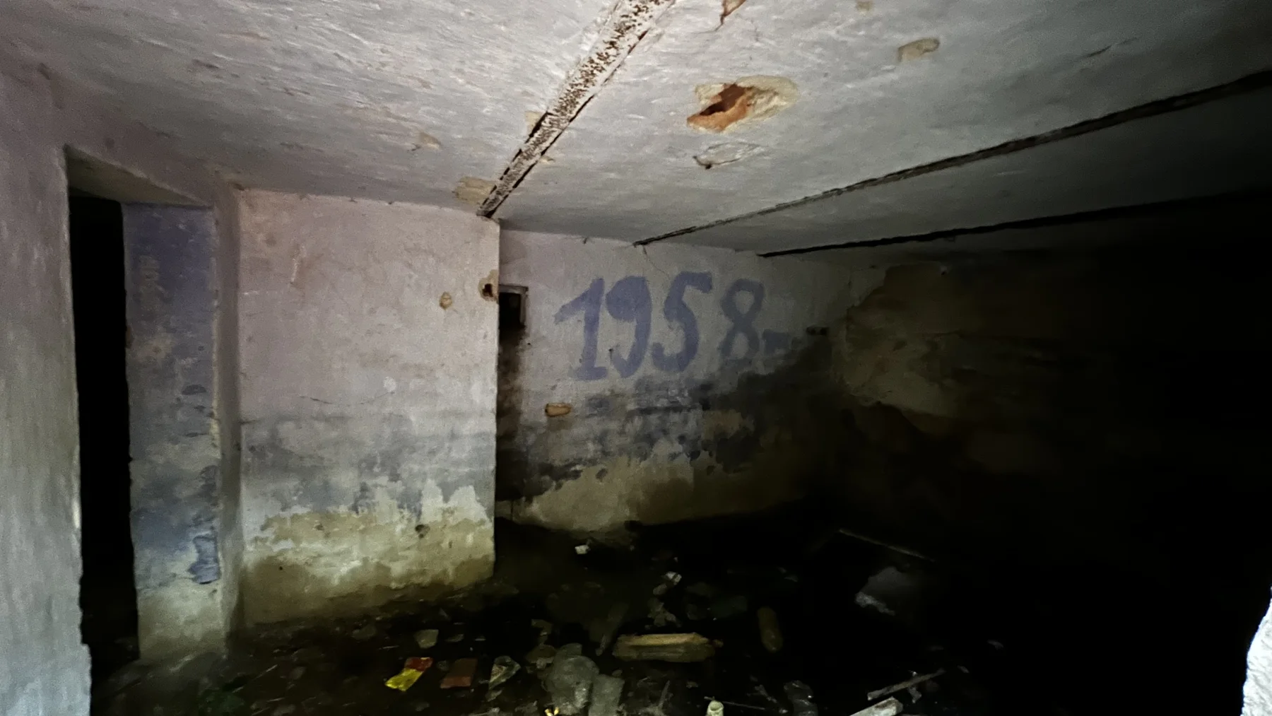 Faded writing marks the wall of a low-ceilinged, shadowy room with rubble below.