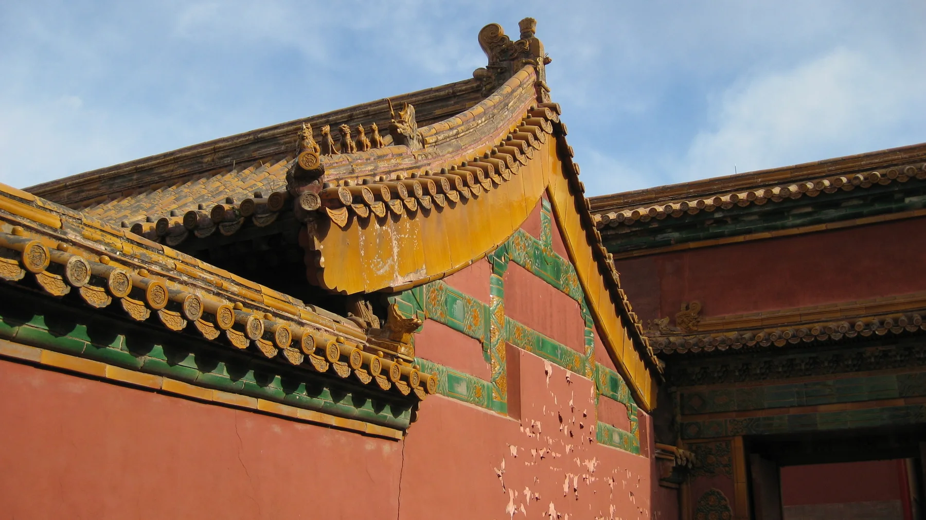 Golden-tiled roof edges overlap above a red wall with green glazed decoration, beneath a patch of blue sky.