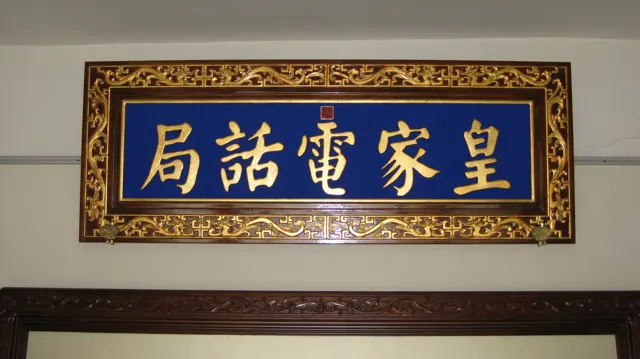 Gold Chinese characters appear on a deep blue sign surrounded by an ornate gold frame above a doorway.