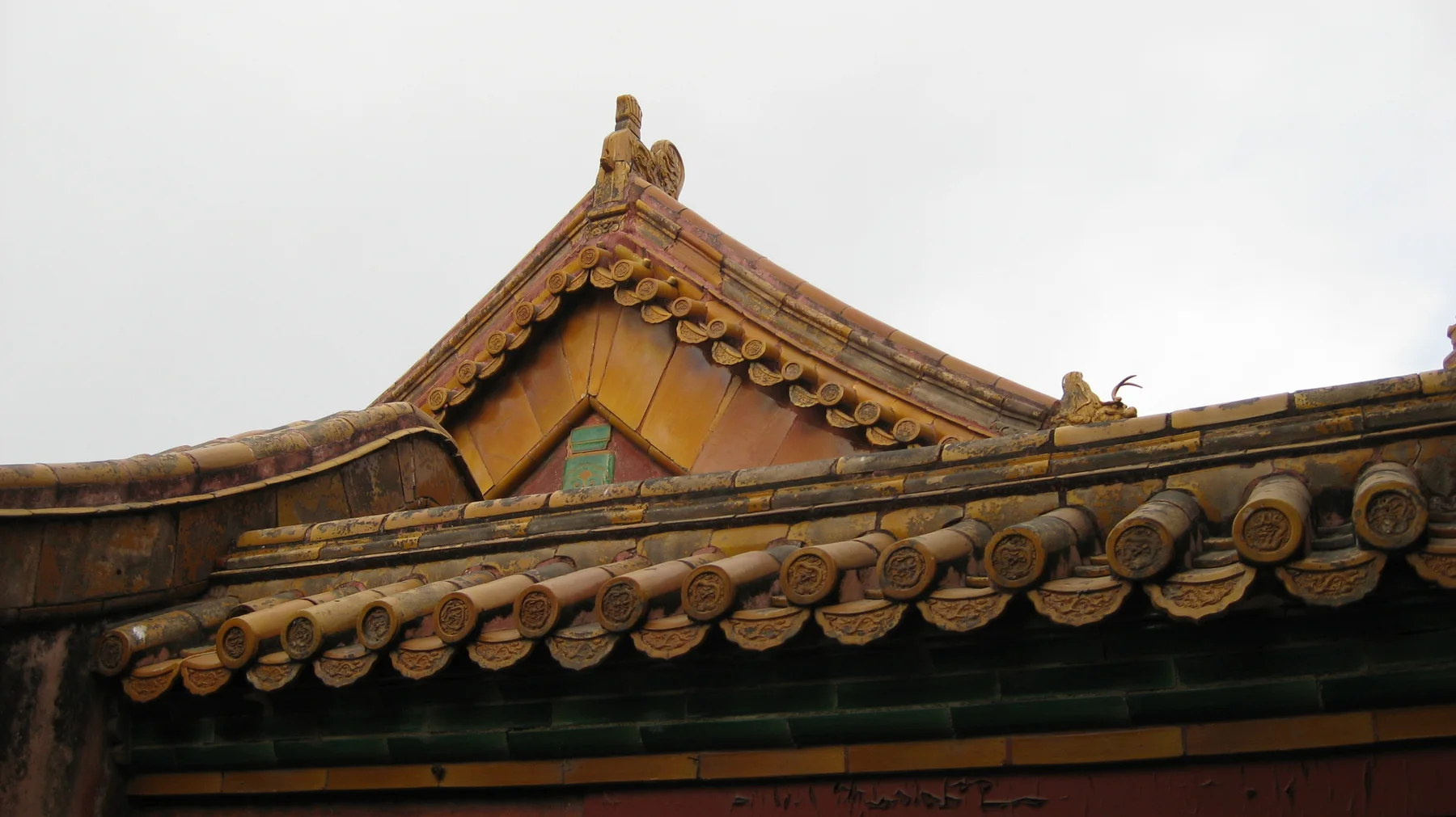 A curved tiled ridge rises behind a lower line of round tile ends, with small roof ornaments against a pale sky.